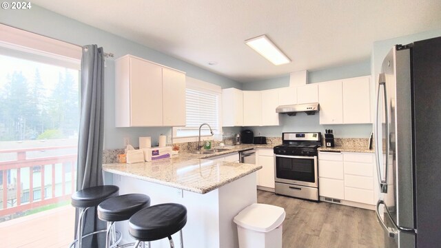 kitchen featuring sink, white cabinetry, light hardwood / wood-style floors, kitchen peninsula, and appliances with stainless steel finishes