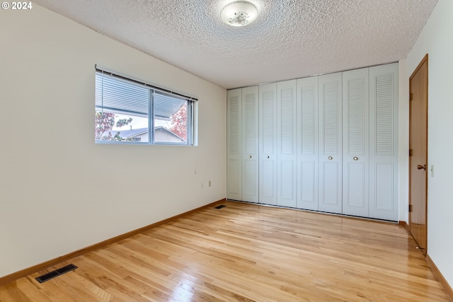 unfurnished bedroom featuring light hardwood / wood-style floors, a textured ceiling, and a closet