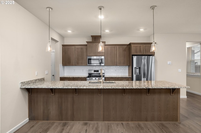 kitchen featuring light stone counters, appliances with stainless steel finishes, and decorative light fixtures