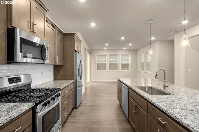 kitchen featuring pendant lighting, sink, stainless steel appliances, light stone counters, and light wood-type flooring