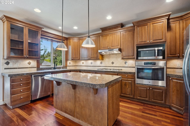 kitchen featuring sink, dark wood-type flooring, stainless steel appliances, a center island, and decorative light fixtures