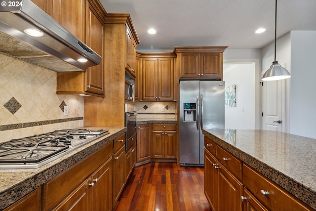 kitchen with appliances with stainless steel finishes, pendant lighting, range hood, tasteful backsplash, and dark hardwood / wood-style flooring