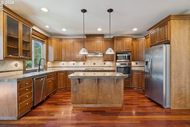 kitchen with sink, stainless steel appliances, a kitchen island, dark hardwood / wood-style flooring, and decorative light fixtures