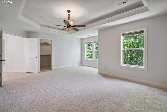 unfurnished bedroom featuring a spacious closet, light carpet, ceiling fan, and a tray ceiling