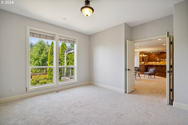 unfurnished room with light colored carpet and a notable chandelier