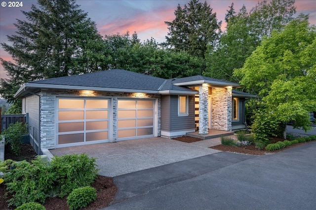 view of front of house with a garage, stone siding, a shingled roof, and concrete driveway