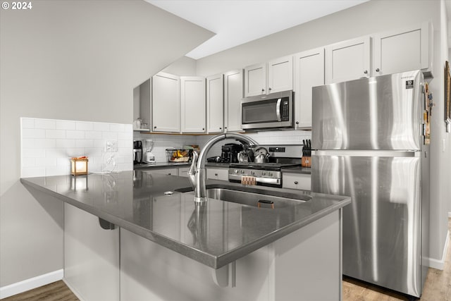 kitchen with white cabinets, appliances with stainless steel finishes, kitchen peninsula, and light hardwood / wood-style flooring