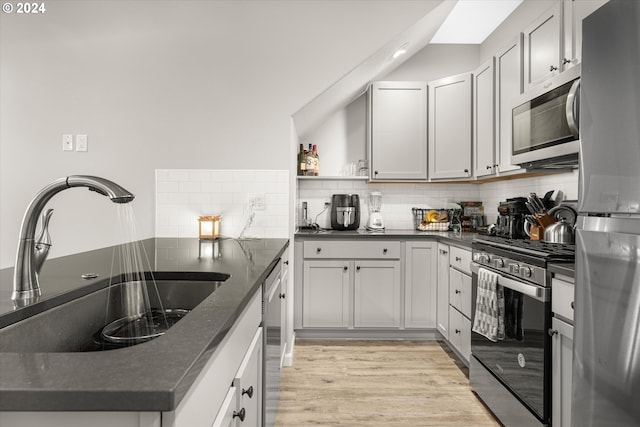 kitchen featuring light hardwood / wood-style floors, dark stone countertops, sink, decorative backsplash, and appliances with stainless steel finishes