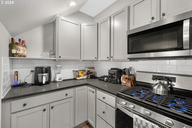 kitchen with backsplash, white cabinetry, vaulted ceiling, appliances with stainless steel finishes, and a textured ceiling