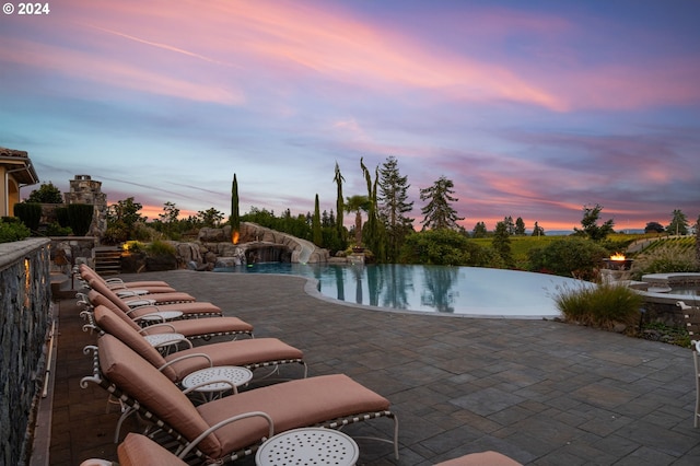 pool at dusk with pool water feature and a patio area