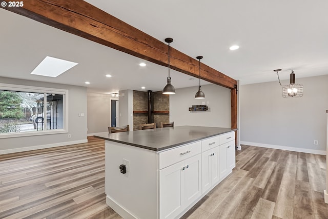 kitchen featuring hanging light fixtures, a skylight, light hardwood / wood-style flooring, beam ceiling, and white cabinetry