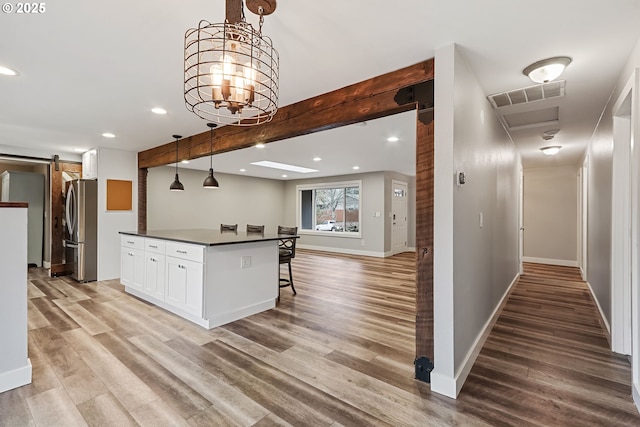 kitchen featuring stainless steel refrigerator, a barn door, beamed ceiling, pendant lighting, and white cabinets