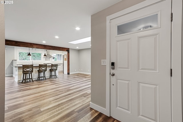 interior space with a breakfast bar area, a skylight, light hardwood / wood-style flooring, and wall chimney exhaust hood