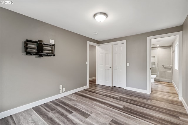 unfurnished bedroom featuring hardwood / wood-style floors, ensuite bath, and a closet