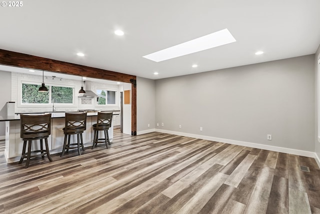 kitchen featuring a skylight, wall chimney range hood, pendant lighting, a center island, and a breakfast bar area