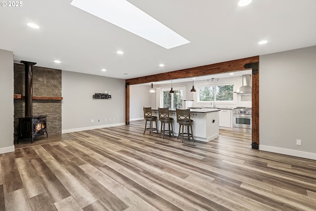 kitchen featuring a wood stove, a kitchen breakfast bar, wall chimney range hood, stainless steel stove, and white cabinetry