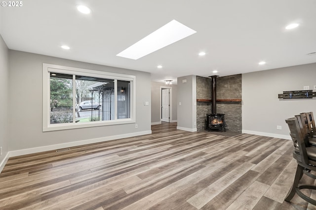 unfurnished living room with wood-type flooring, a wood stove, and a skylight