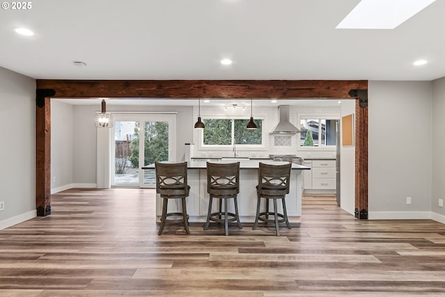 kitchen with wall chimney exhaust hood, a breakfast bar, decorative light fixtures, light hardwood / wood-style floors, and white cabinetry