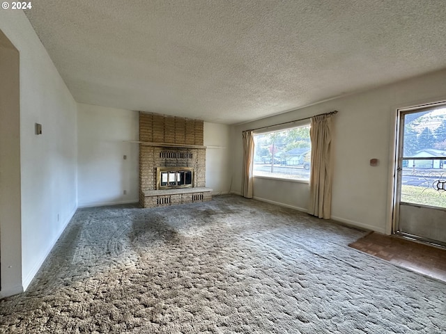 unfurnished living room with carpet flooring, a textured ceiling, and a brick fireplace