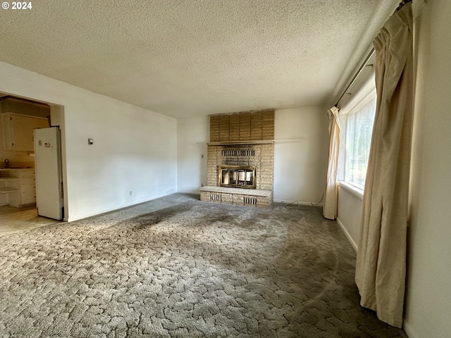 unfurnished living room with carpet flooring, a textured ceiling, and a brick fireplace