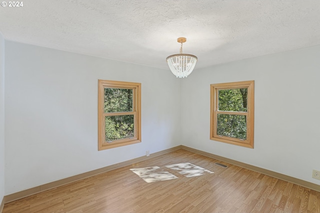 unfurnished room with a notable chandelier, hardwood / wood-style floors, and a textured ceiling