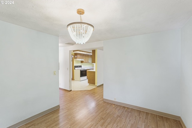 spare room featuring light hardwood / wood-style flooring, a textured ceiling, and an inviting chandelier