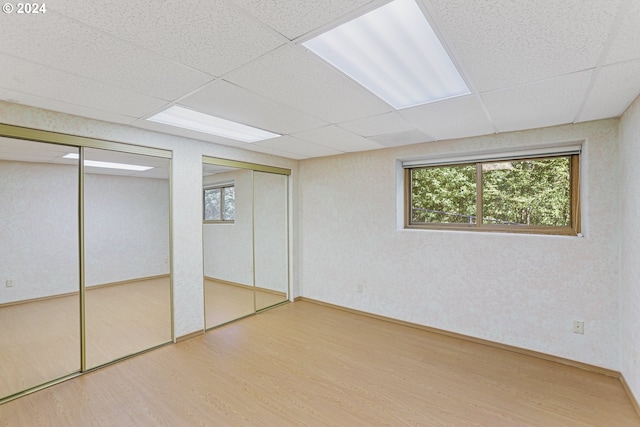 unfurnished bedroom with a drop ceiling, two closets, and wood-type flooring