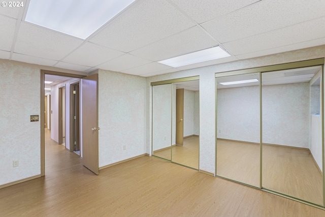 unfurnished bedroom featuring a drop ceiling, hardwood / wood-style flooring, and two closets