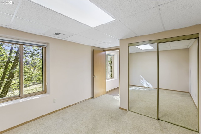 unfurnished bedroom with light carpet, a closet, and a paneled ceiling