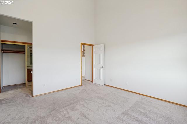 unfurnished bedroom featuring a towering ceiling, light colored carpet, and a closet