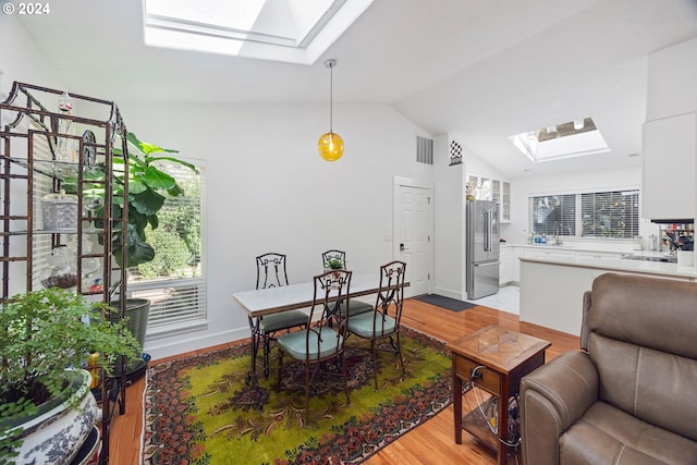 dining room with light hardwood / wood-style floors and lofted ceiling with skylight