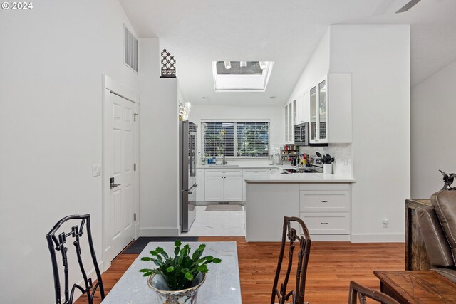 kitchen featuring white cabinetry, light hardwood / wood-style flooring, stainless steel appliances, decorative backsplash, and lofted ceiling with skylight