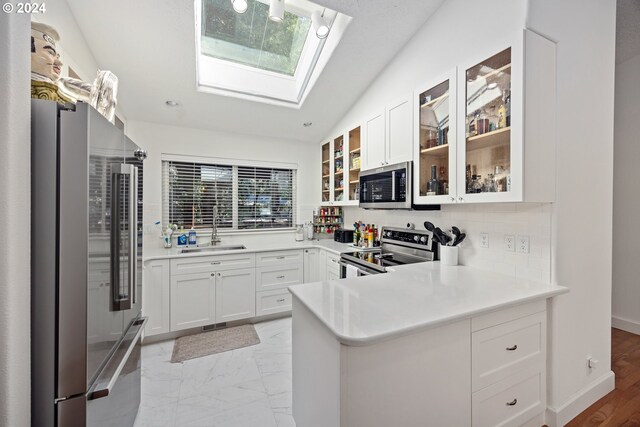 kitchen featuring sink, appliances with stainless steel finishes, lofted ceiling with skylight, and white cabinetry