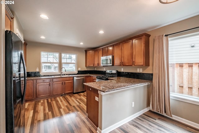 kitchen featuring light hardwood / wood-style floors, kitchen peninsula, stainless steel appliances, and dark stone counters