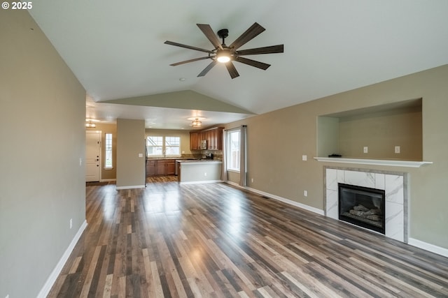 unfurnished living room featuring dark wood-style floors, lofted ceiling, a high end fireplace, and baseboards