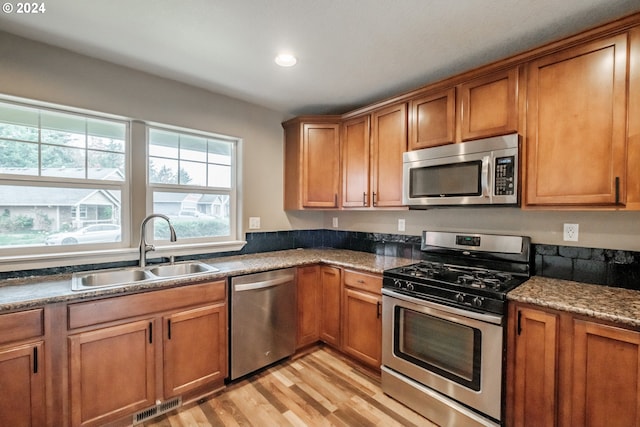 kitchen with stainless steel appliances, light hardwood / wood-style flooring, dark stone counters, and sink