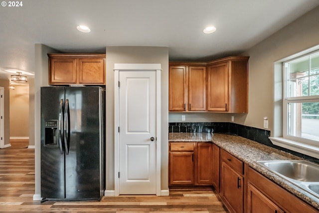 kitchen featuring light hardwood / wood-style flooring, black fridge, dark stone counters, and sink