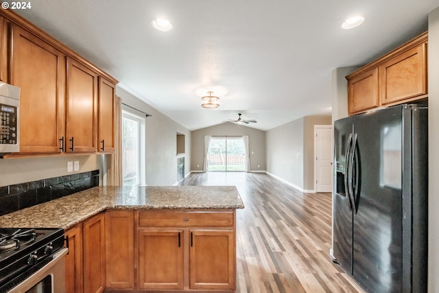 kitchen with light stone countertops, ceiling fan, light hardwood / wood-style floors, vaulted ceiling, and black fridge with ice dispenser