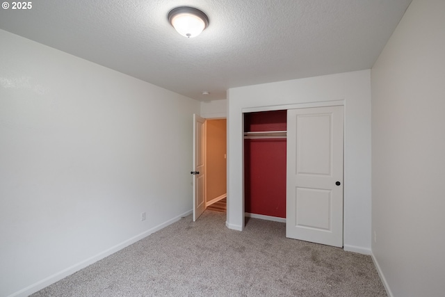 unfurnished bedroom with a closet, light carpet, a textured ceiling, and baseboards