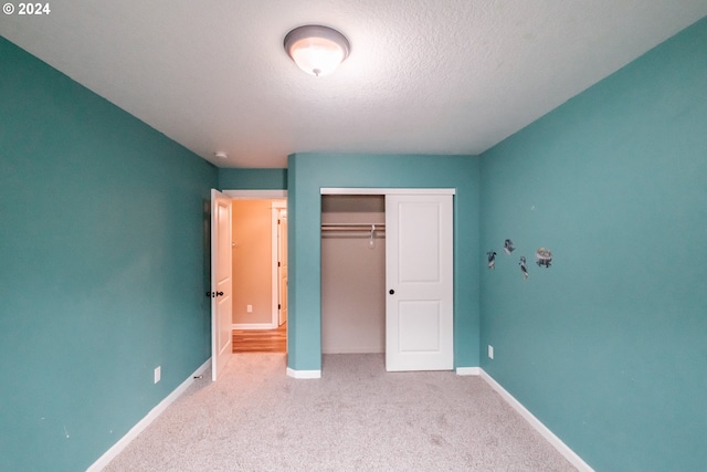 unfurnished bedroom featuring light carpet, a closet, and a textured ceiling