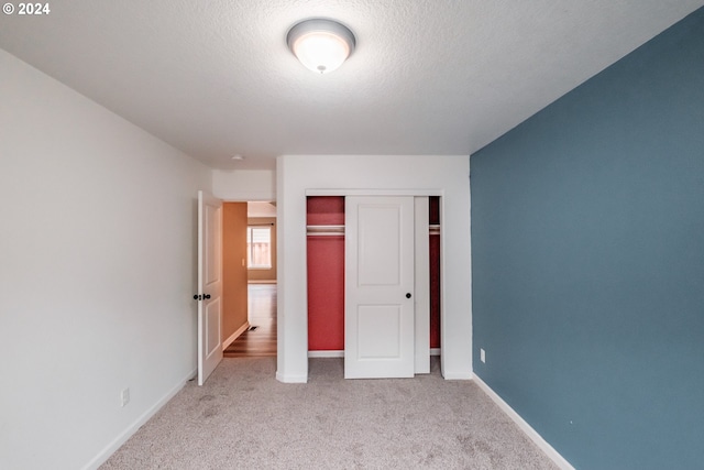 unfurnished bedroom featuring a textured ceiling, light carpet, and a closet