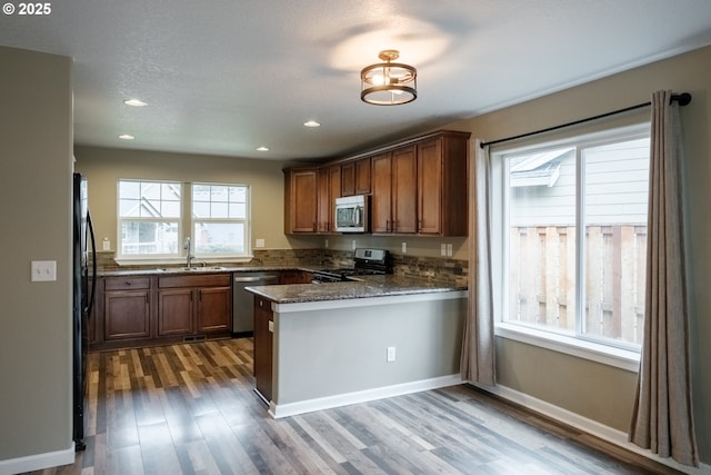 kitchen featuring brown cabinetry, dark stone countertops, a peninsula, stainless steel appliances, and a sink