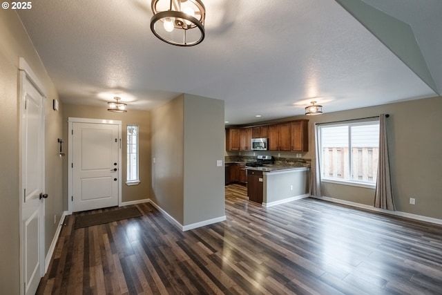 kitchen featuring baseboards, appliances with stainless steel finishes, brown cabinets, dark wood-type flooring, and a peninsula