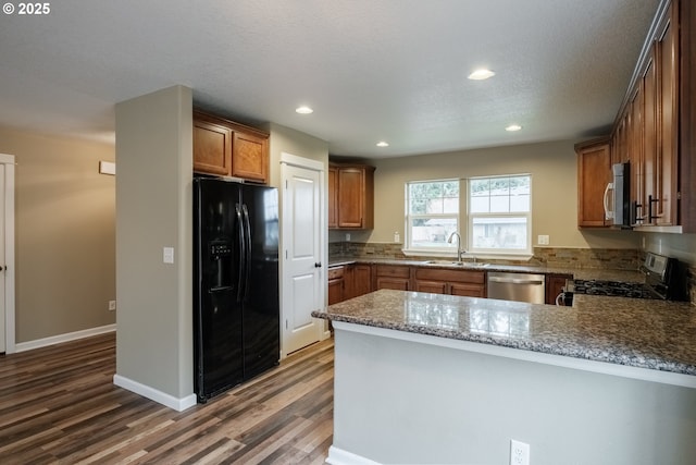 kitchen featuring stone countertops, brown cabinets, a peninsula, stainless steel appliances, and a sink