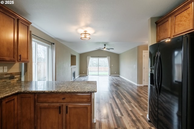 kitchen with brown cabinets, vaulted ceiling, black refrigerator with ice dispenser, and open floor plan