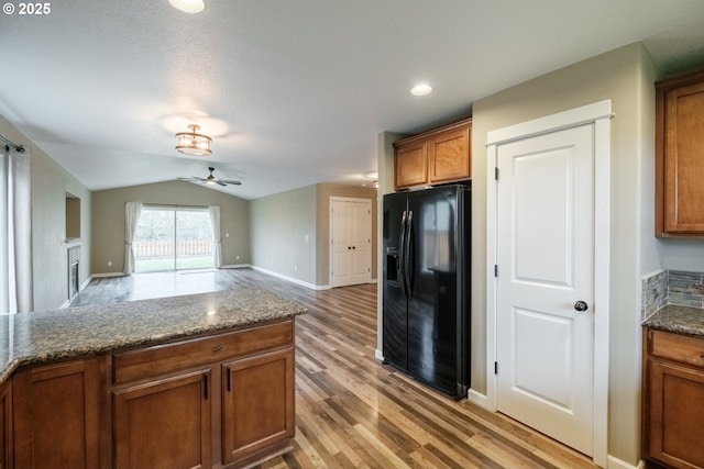 kitchen with dark stone counters, lofted ceiling, brown cabinets, open floor plan, and black refrigerator with ice dispenser