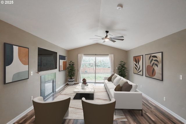 living room featuring baseboards, a tiled fireplace, dark wood-style floors, ceiling fan, and vaulted ceiling