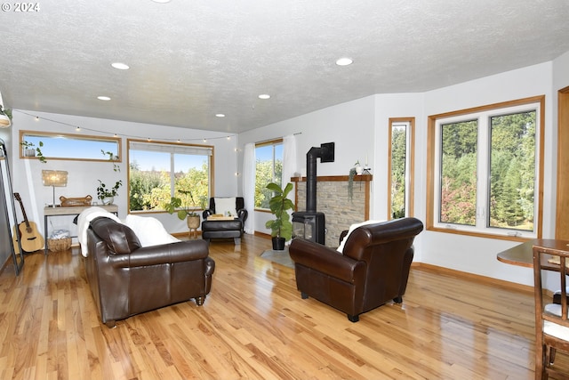 living room with a wealth of natural light, light hardwood / wood-style floors, a textured ceiling, and a wood stove