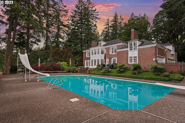 pool at dusk with a diving board and a water slide