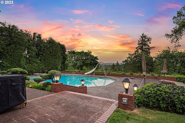 pool at dusk featuring a patio area, a diving board, and a water slide